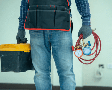 A worker carrying tools and parts for an HVAC system.